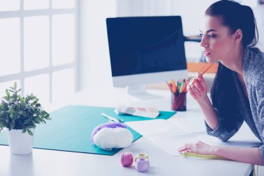 Moda tasarımcıları stüdyoda çalışıyor, masanın yanında duruyorlar.