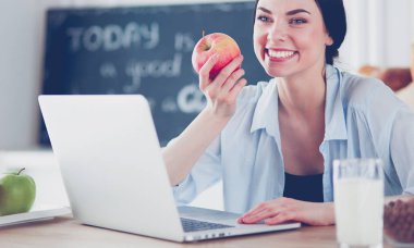 Elma ve dizüstü bilgisayar mutfakta oturan kadın