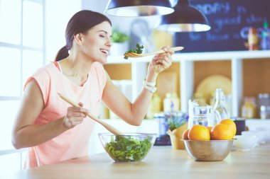 Gülümseyen genç kadın mutfakta taze salata karıştırıyor..