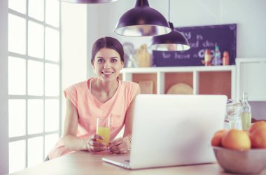 Mutfakta dizüstü bilgisayara benzeyen tariflerle gülümseyen genç bir kadın. Gıda blogcusu kavramı