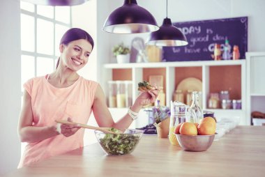 Gülümseyen genç kadın mutfakta taze salata karıştırıyor..