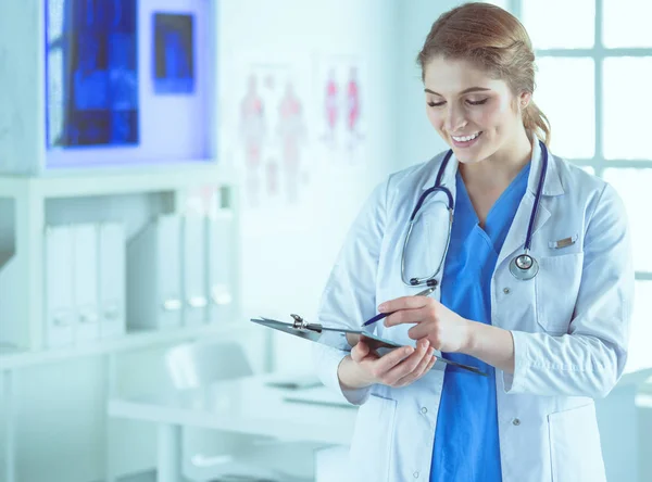 Doctor con un estetoscopio, sosteniendo un cuaderno en su mano. Primer plano de una doctora llenando el formulario médico en el portapapeles mientras está de pie en el hospital —  Fotos de Stock