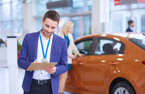 Obchodník se ženou stojí v blízkosti nového auta v showroomu — Stock fotografie