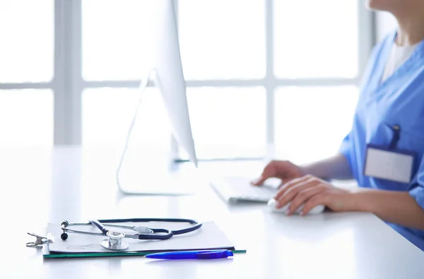 Schöne junge lächelnde Ärztin sitzt am Schreibtisch — Stockfoto