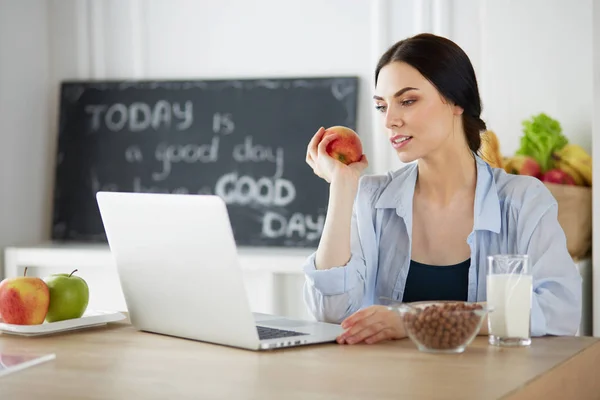 Donna con mela e laptop seduta in cucina — Foto Stock