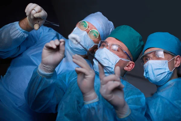 Grupo de cirurgiões no trabalho em sala de operações tonificada em azul. Equipe médica realizando operação — Fotografia de Stock