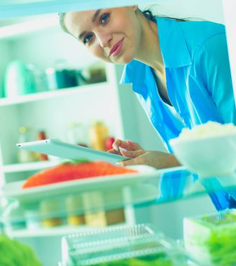 Sağlıklı yiyecek, sebze ve meyvelerle dolu açık buzdolabının yanında duran kadın portresi..