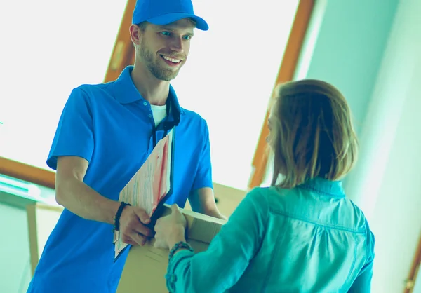 Lachende bezorger in blauw uniform levert pakketdoos aan ontvanger - koerier service concept. Glimlachende bezorger in blauw uniform — Stockfoto