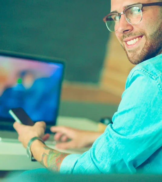 Jonge man met telefoon en werkt op de laptop. — Stockfoto