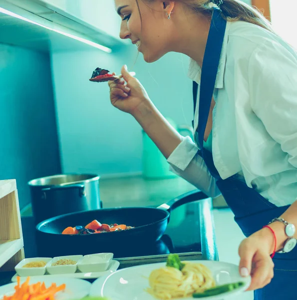 Νεαρή γυναίκα στέκεται δίπλα στη σόμπα στην κουζίνα — Φωτογραφία Αρχείου