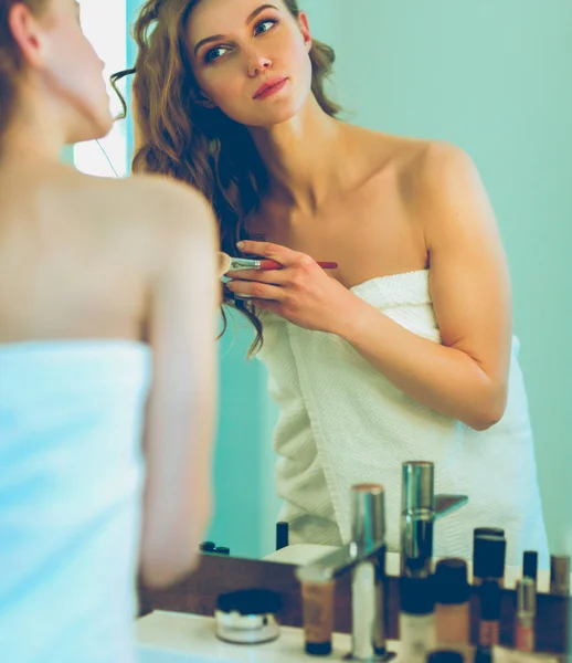 Mujer joven mirándose en el espejo en el baño . — Foto de Stock