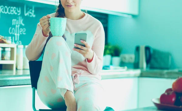 Kvinna med mobiltelefon sitter i moderna kök. — Stockfoto