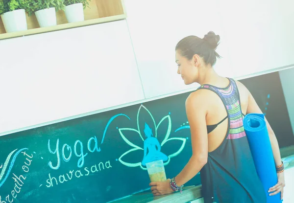 Retrato de una mujer sonriente sosteniendo en su mano una esterilla de yoga mientras estaba de pie en el estudio. Yoga. Una mujer. Bienestar — Foto de Stock