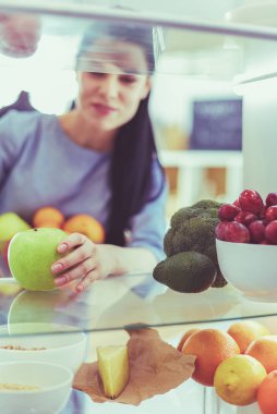 Gülümseyen kadın buzdolabından taze meyve alıyor, sağlıklı yiyecek konsepti.