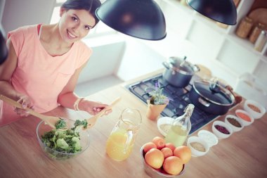 Gülümseyen genç kadın mutfakta taze salata karıştırıyor..