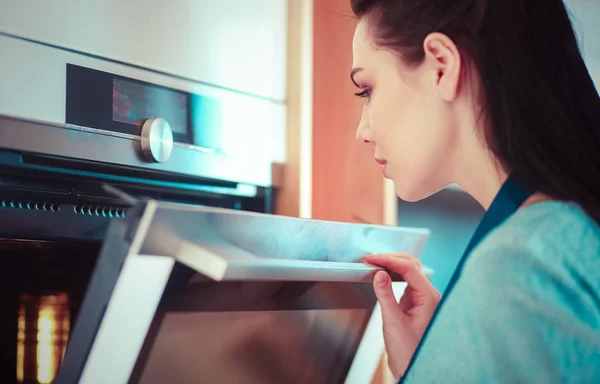 Mulher bonita verificando como seu bolo está indo no forno — Fotografia de Stock