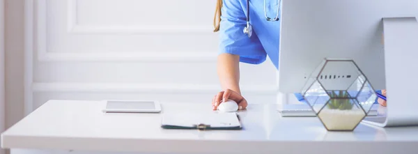 Portrait of female physician using laptop computer while standing near reception desk at clinic or emergency hospital