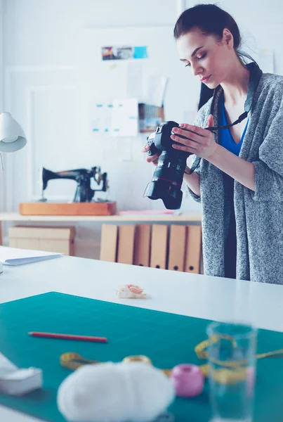 Jonge vrouw ontwerper staat in de buurt van de werkplek en fotograferen op digitale camera — Stockfoto