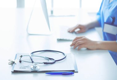 Kadın doktor masada oturuyor ve hastanede dizüstü bilgisayarla çalışıyor.