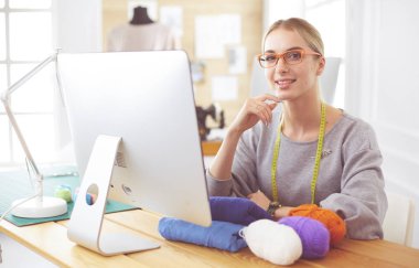 Moda tasarımcısı kadın stüdyoda çalışıyor, masada oturuyor.