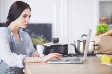 Mutfakta yemek yapmak için tablet bilgisayar kullanan genç bir kadın..