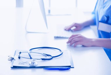 Kadın doktor masada oturuyor ve hastanede dizüstü bilgisayarla çalışıyor.