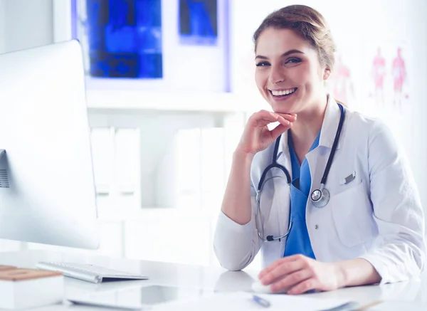 Young female doctor sitting at a desk and working on the computer at the hospital office. Health care, insurance and help concept. Physician ready to examine patient — Stock Photo, Image