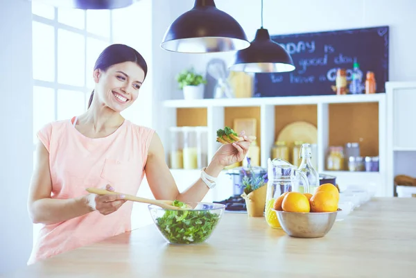 Gülümseyen genç kadın mutfakta taze salata karıştırıyor..