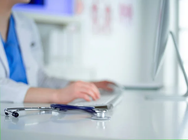 Close-up of stethoscope is lying on the table near female doctor typing on laptop computer — Stock Photo, Image
