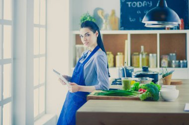 Mutfakta yemek yapmak için tablet bilgisayar kullanan genç bir kadın.
