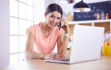 Mutfakta dizüstü bilgisayara benzeyen tariflerle gülümseyen genç bir kadın. Gıda blogcusu kavramı