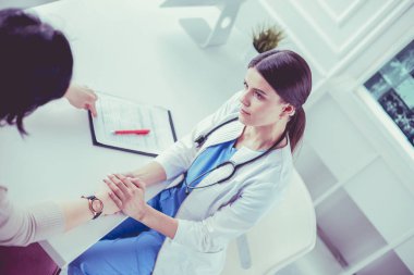 Kadın doktor hastane danışma odasında bir hastayı sakinleştiriyor, elini tutuyor.