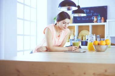 Mutfakta dijital tablet kullanan güzel genç bir kadın.