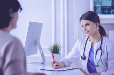 Doktor ve hasta hastane danışma odasında tıbbi sorunları tartışıyorlar. Doktor hasta formunu dolduruyor.