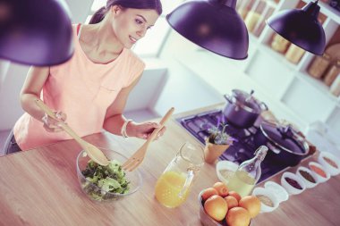 Gülümseyen genç kadın mutfakta taze salata karıştırıyor..