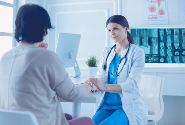 Kadın doktor hastane danışma odasında bir hastayı sakinleştiriyor, elini tutuyor.