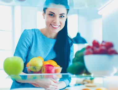 Gülümseyen kadın buzdolabından taze meyve alıyor, sağlıklı yiyecek konsepti.