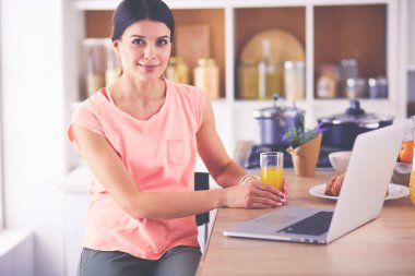 Mutfakta dizüstü bilgisayara benzeyen tariflerle gülümseyen genç bir kadın. Gıda blogcusu kavramı