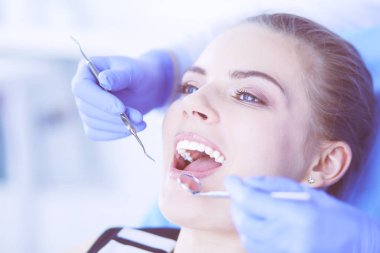 Dişçi muayenehanesinde diş muayenesi yapan ağzı açık genç bir kadın hasta..