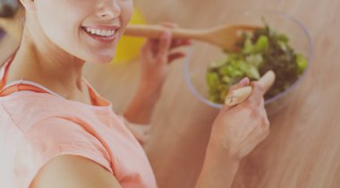 Gülümseyen genç kadın mutfakta taze salata karıştırıyor..