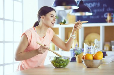 Gülümseyen genç kadın mutfakta taze salata karıştırıyor..