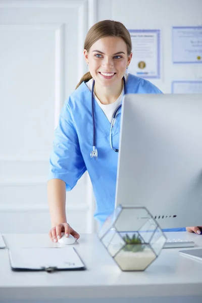 Young doctor woman standing near table, isolated on white background