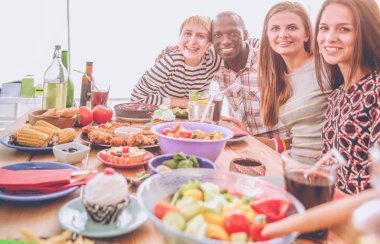 Ahşap masada otururken birlikte yemek yiyen bir grup insanın üst düzey görüntüsü. Masada yemek var. İnsanlar fast food yiyor..