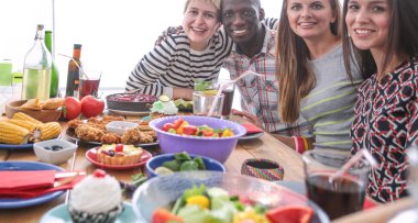 Ahşap masada otururken birlikte yemek yiyen bir grup insanın üst düzey görüntüsü. Masada yemek var. İnsanlar fast food yiyor..