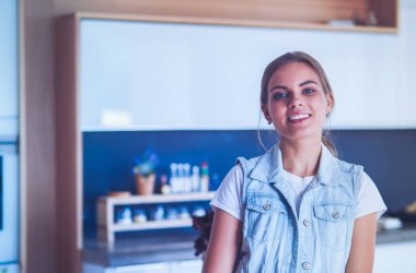 Kollarını mutfak arka planında kavuşturmuş genç bir kadının portresi.