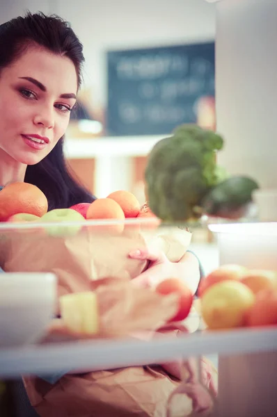 Mosolygó nő vesz egy friss gyümölcsöt ki a hűtőből, egészséges étel koncepció — Stock Fotó