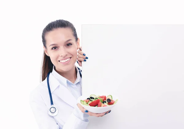 Portrait d'une belle femme médecin tenant une assiette avec des légumes frais debout près de blanc. Femmes médecins — Photo