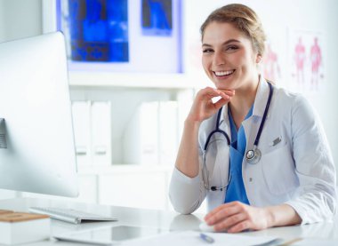 Genç bayan doktor bir masada oturuyor ve hastane ofisindeki bilgisayar üzerinde çalışıyor. Sağlık, sigorta ve yardım konsepti. Doktor hastayı muayene etmeye hazır.