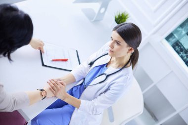 Kadın doktor hastane danışma odasında bir hastayı sakinleştiriyor, elini tutuyor.