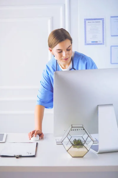 Portrait of female physician filling up medical form while standing near reception desk at clinic or emergency hospital